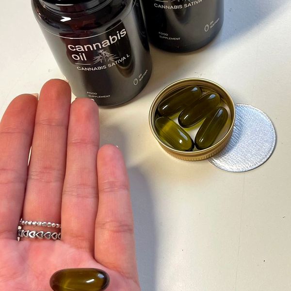 Dlan z mehkimi kapsulami ob temnem kozarčku Cannabis Oil