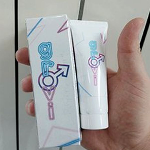 Roka drži belo škatlico in tubo gela Grovi z modro-rožnatim logotipom