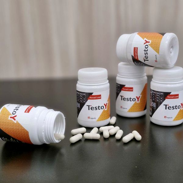 Bele plastenke TestoY s 15 kapsulami in razsute bele kapsule na temni mizi